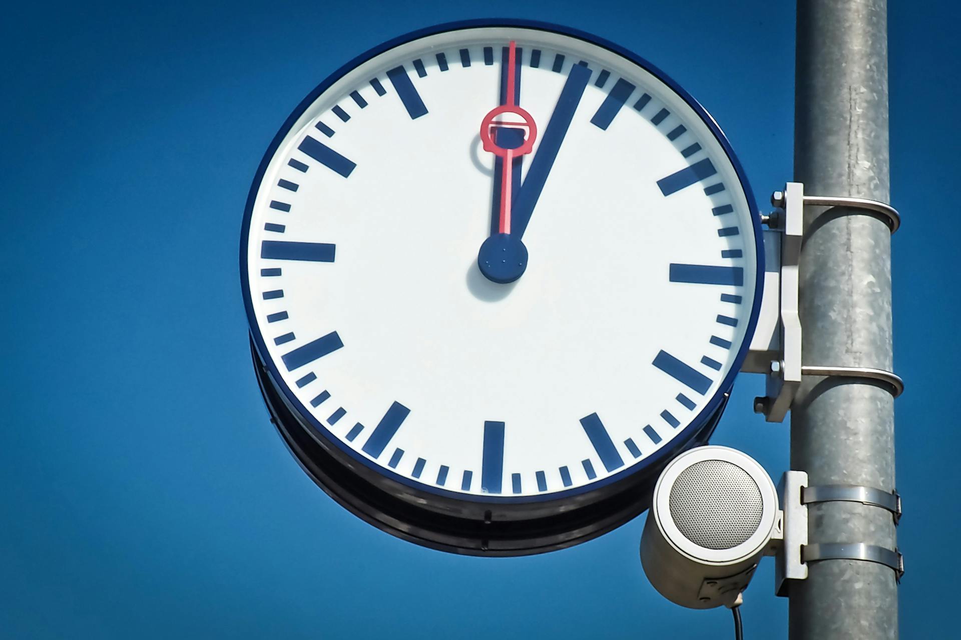 Large analog clock showing one minute to twelve against a clear blue sky, symbolizing urgency, fast response time, and the importance of timely customer service in ecommerce automation.