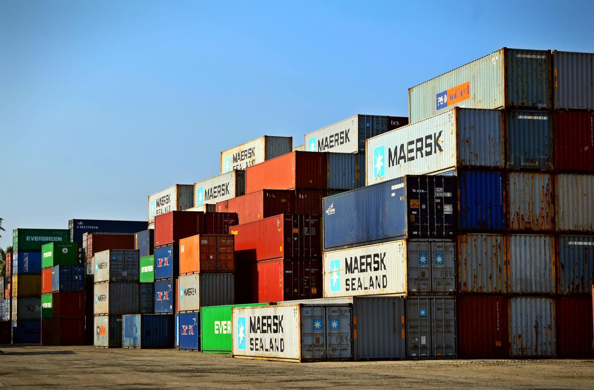 Stacked international shipping containers at a freight yard, representing global logistics, supply chain management, and cross-border ecommerce fulfillment infrastructure.