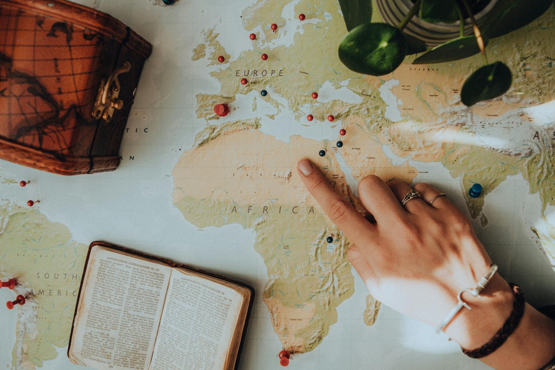 Hand pointing at a location on a world map marked with push pins, representing strategic planning for global market entry and cross-border ecommerce expansion.