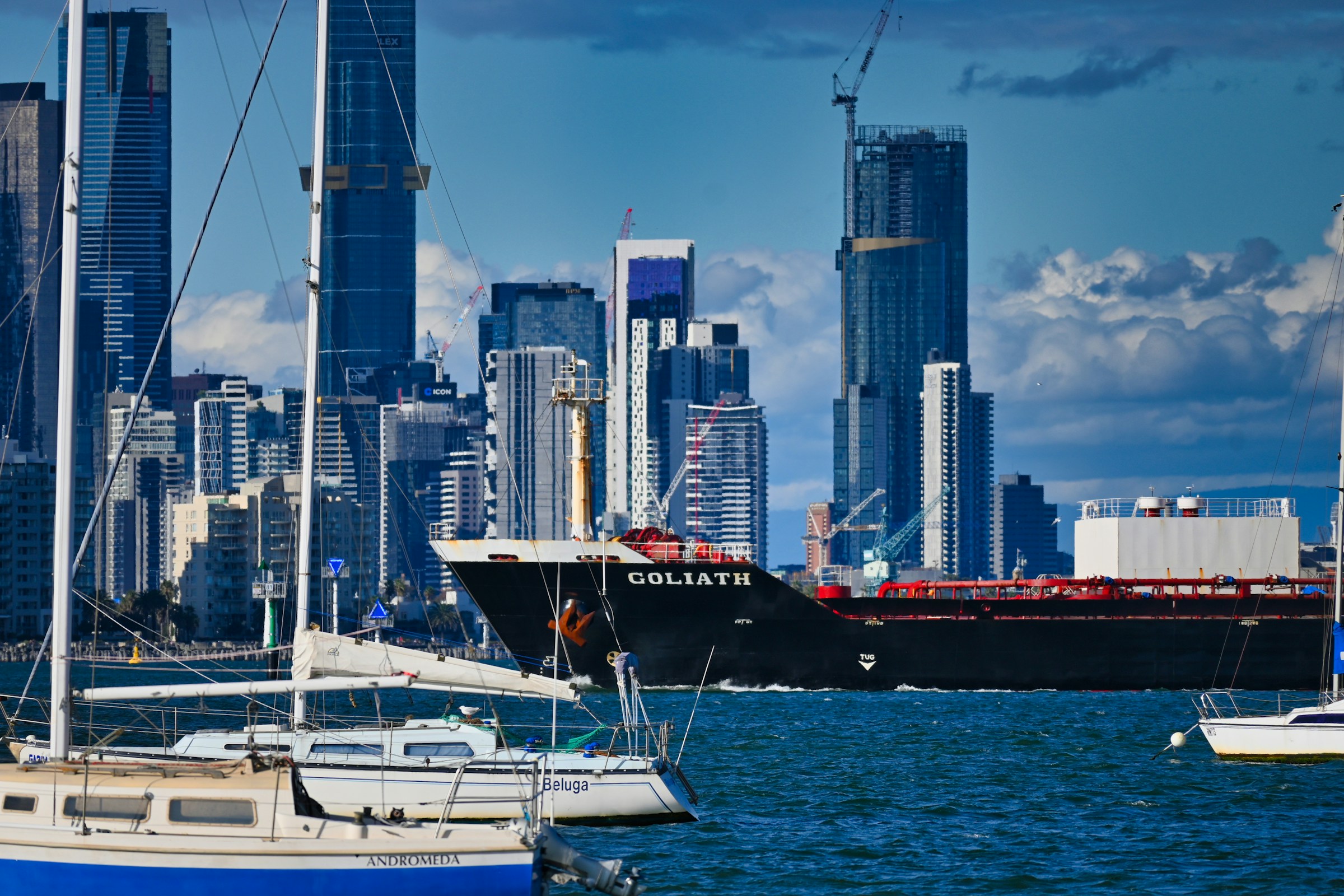 Large cargo ship named Goliath sailing near a modern city skyline, symbolizing urban port logistics, international shipping, and global freight transport infrastructure.