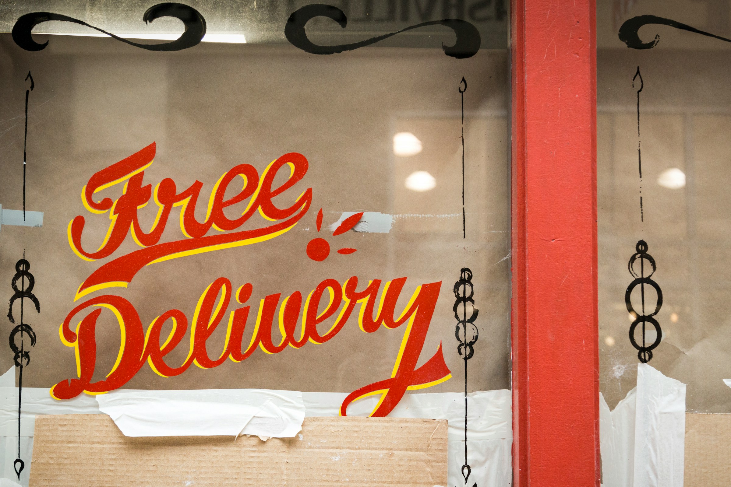 Hand-painted ‘Free Delivery’ sign on a storefront window, representing ecommerce shipping incentives, flat rate shipping alternatives, and free shipping promotions for online retailers.