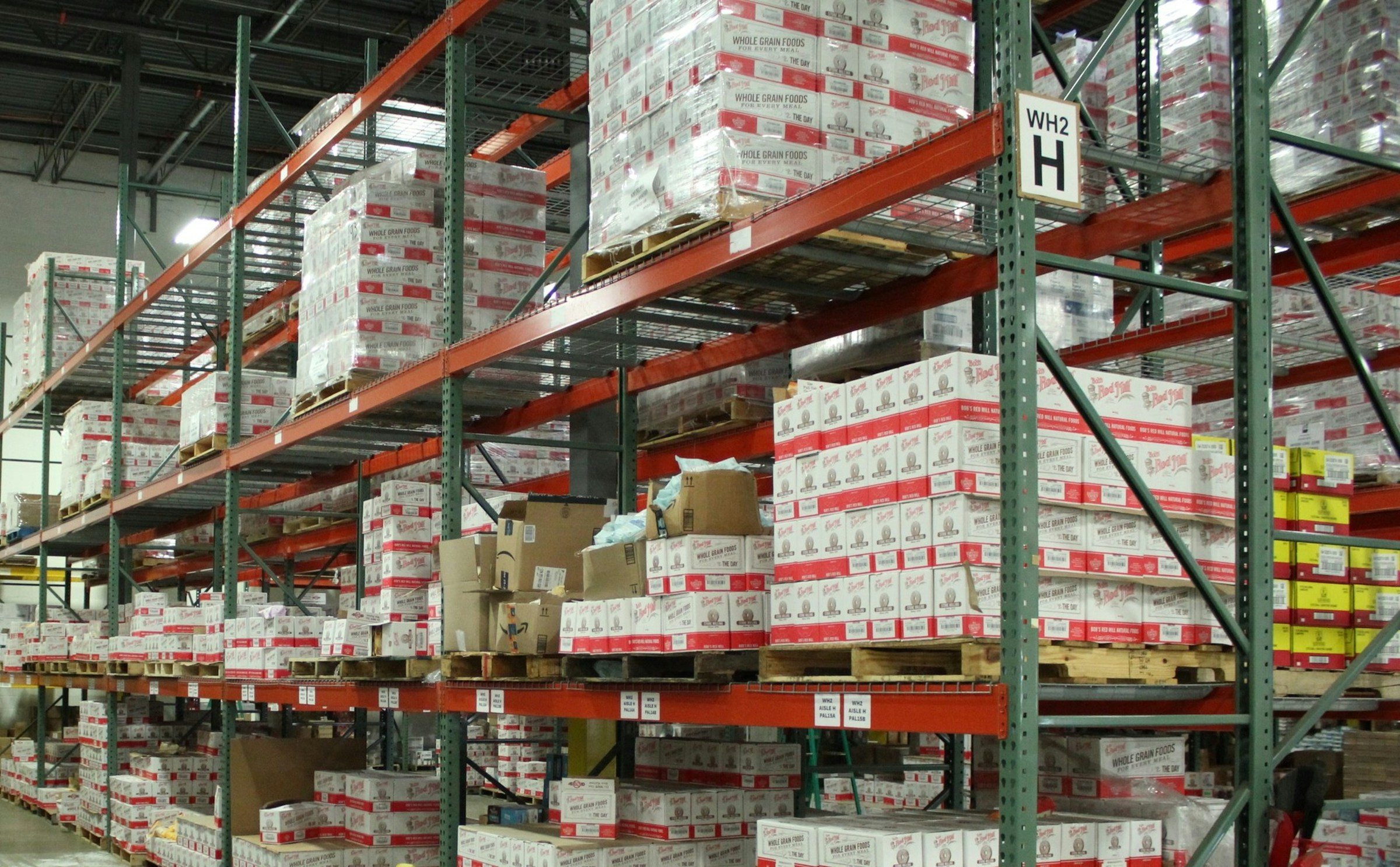 Large warehouse with stacked pallets of packaged goods, representing ecommerce fulfillment center operations, inventory management, and bulk shipping logistics for online retailers.