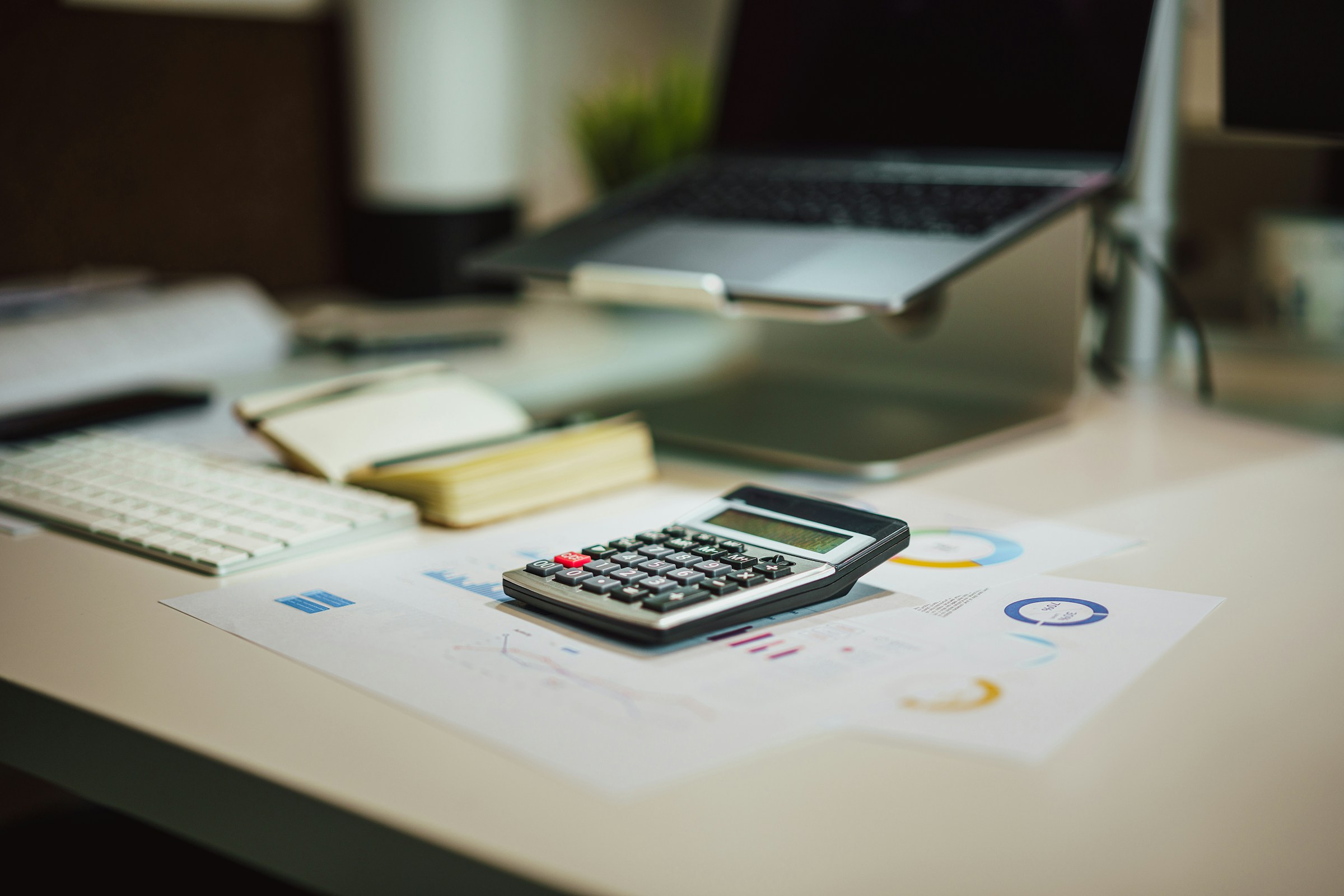 Close-up of a calculator on a desk with financial charts and a laptop, representing ecommerce shipping costs, budgeting, and international delivery rate calculations.
