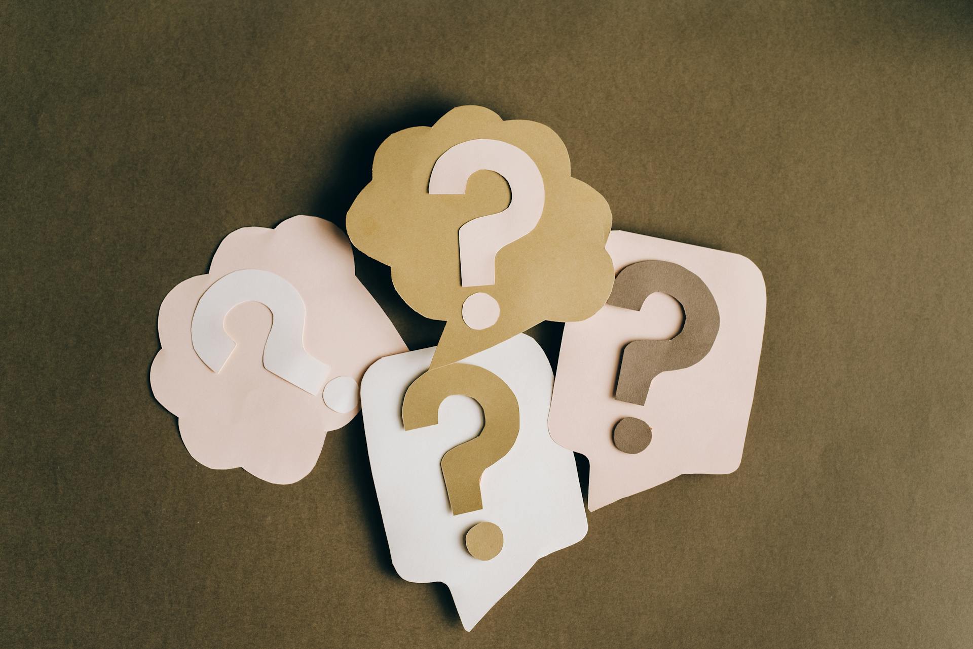 Paper cutouts of question marks inside chat bubbles on a neutral background, representing frequently asked questions (FAQs) and automated customer support queries in ecommerce.