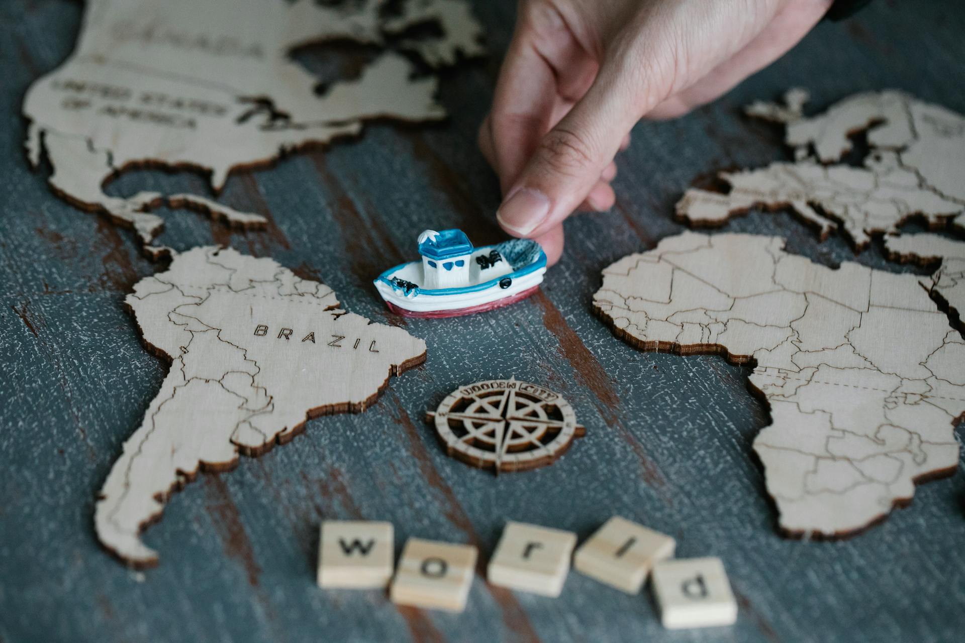 Hand placing a toy boat between wooden cutouts of world continents labeled Brazil and Africa, symbolizing international trade, global shipping, and cross-border ecommerce logistics.