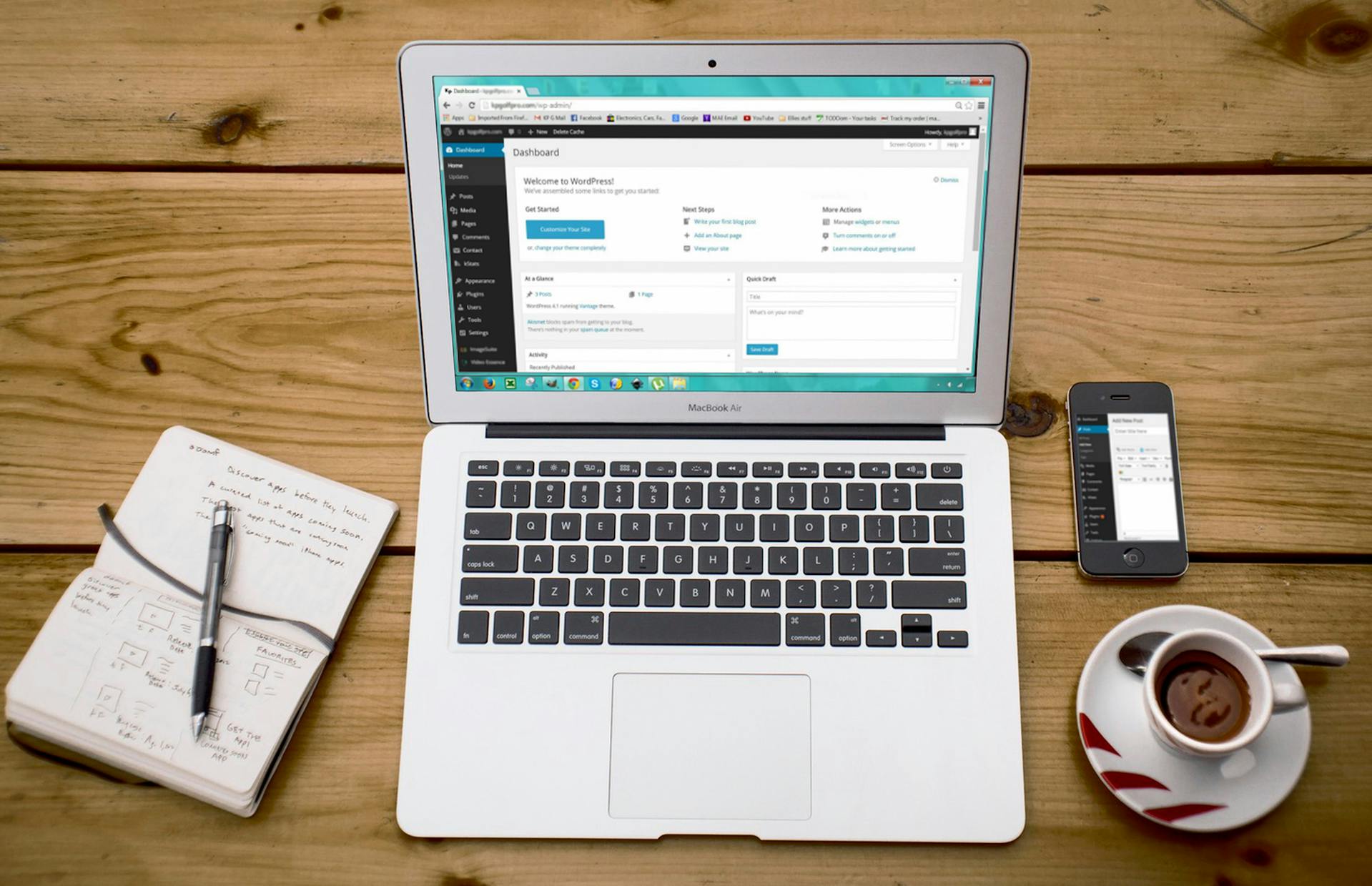 Laptop with WordPress dashboard open, smartphone, notebook, and coffee cup on a wooden desk—representing website content management, SEO optimization, and digital marketing workflow.