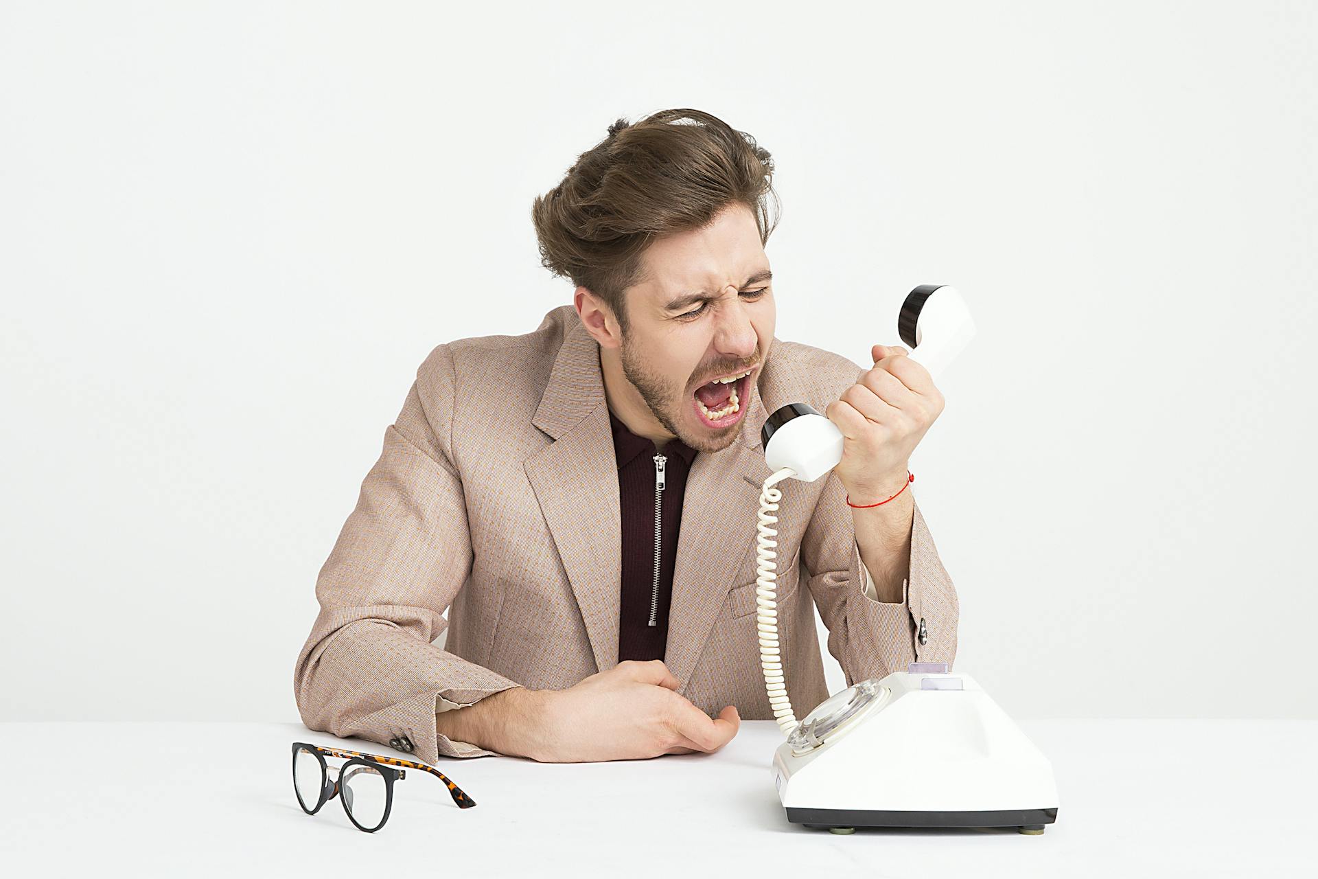 Frustrated customer yelling into a rotary phone, representing poor customer service experience and lack of effective support communication.